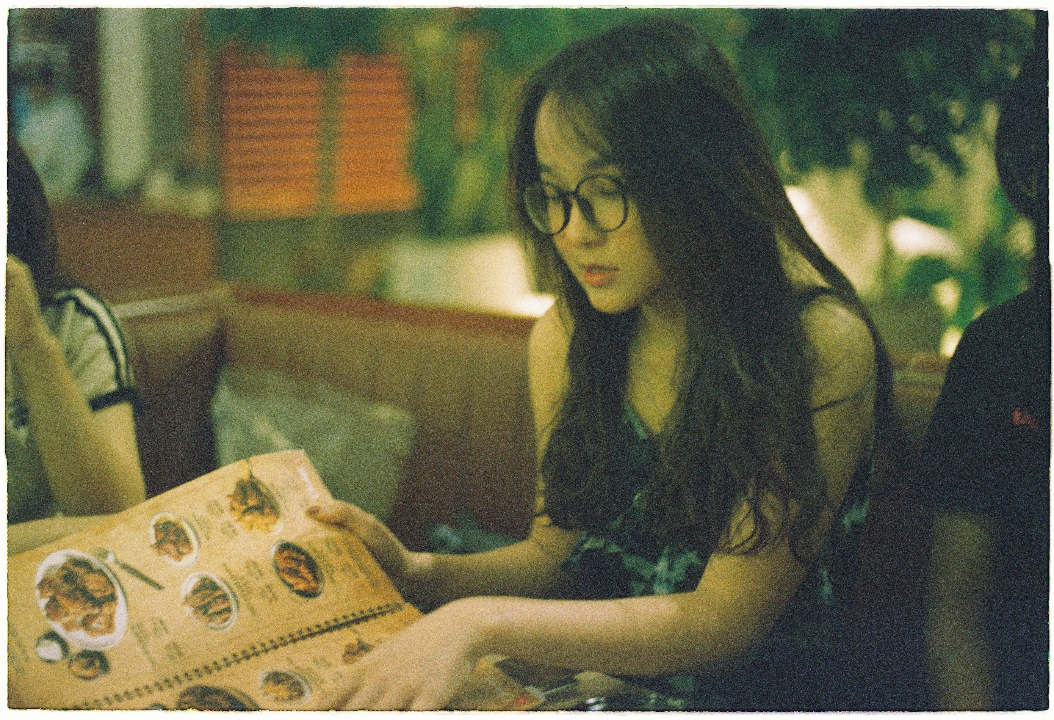 Woman with glasses browsing a menu in a cozy restaurant, puzzling over the options