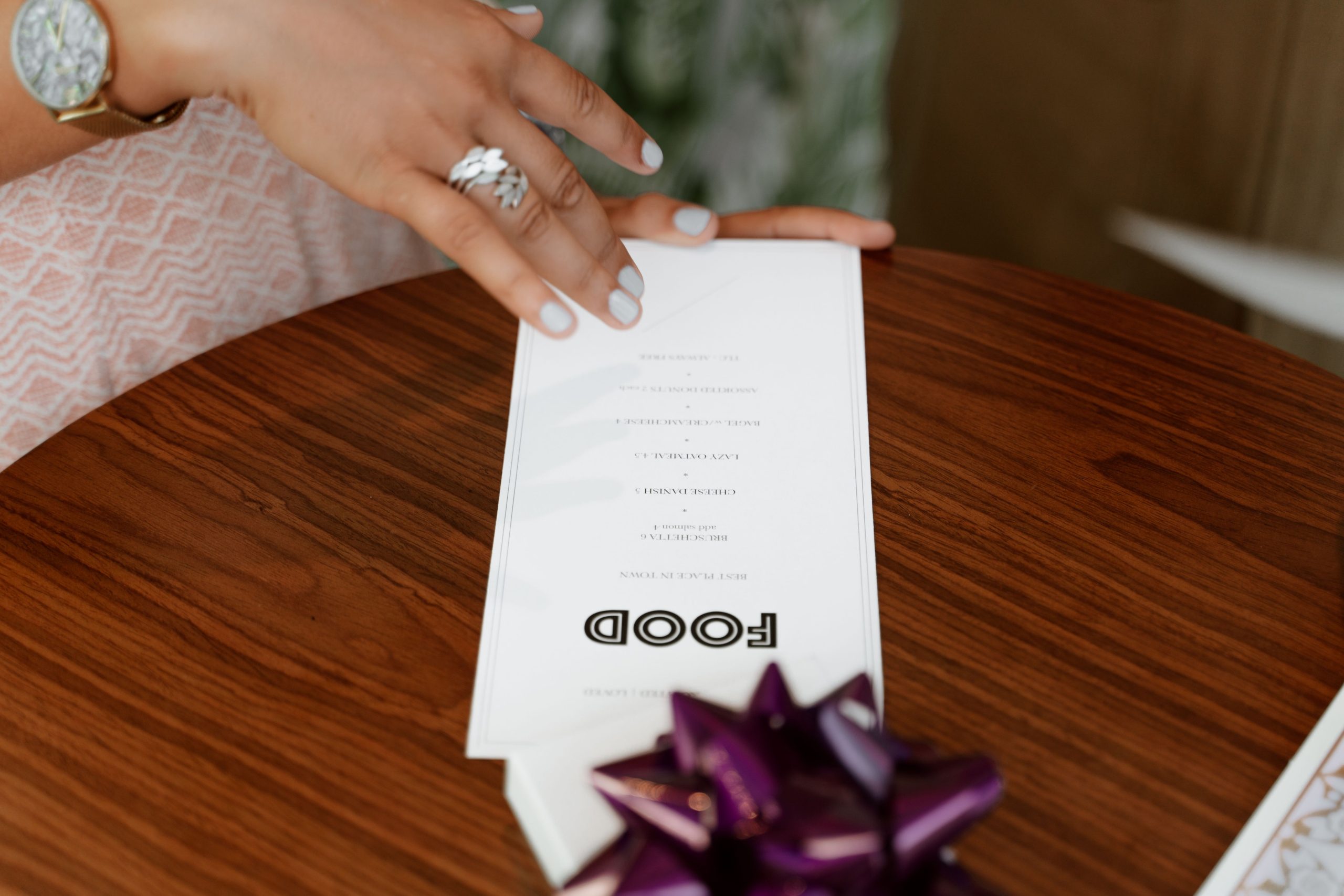 Close-up of a hand holding a restaurant menu on a wooden table with elegant decor